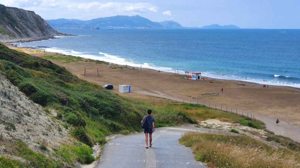 Relaxing coastal view in Bilbao, featuring cliffs, waves, and a lone walker by the shore.