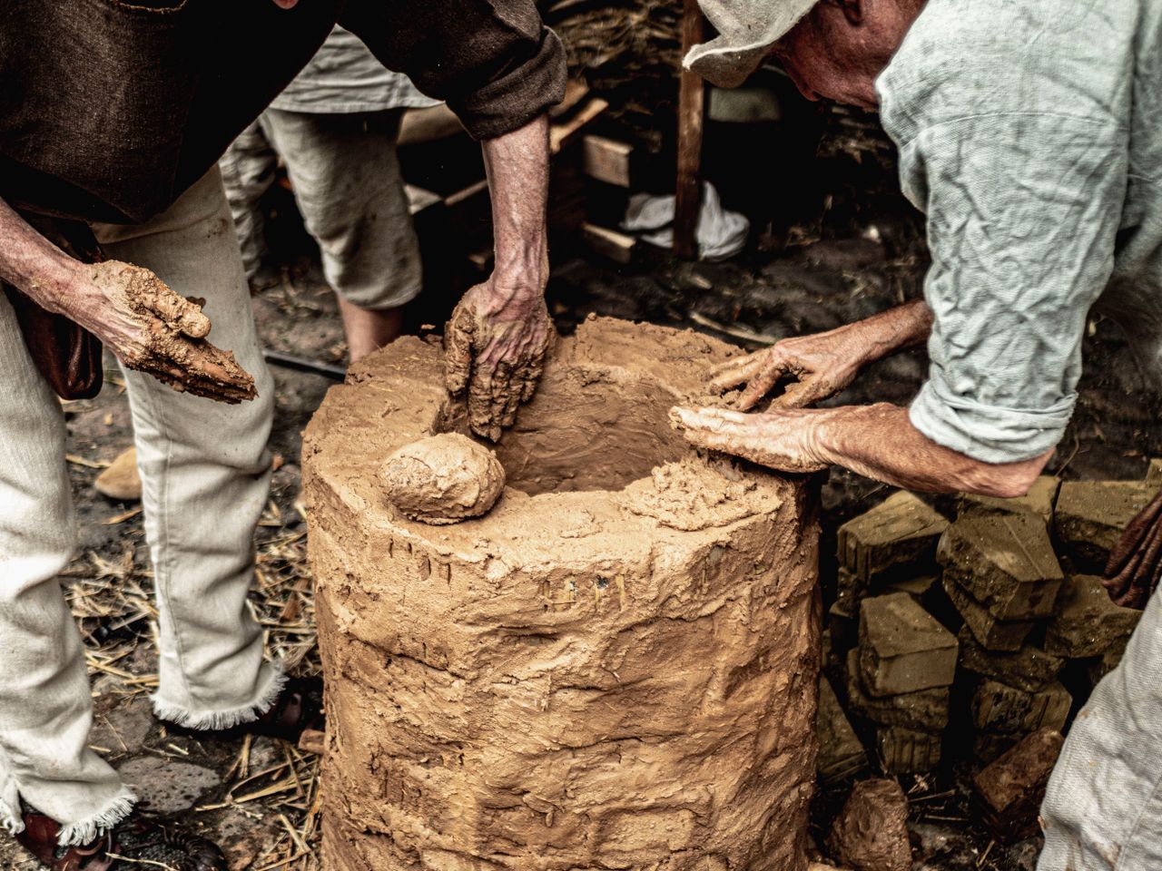 People building a traditional clay oven using hands, showcasing craftsmanship and teamwork.